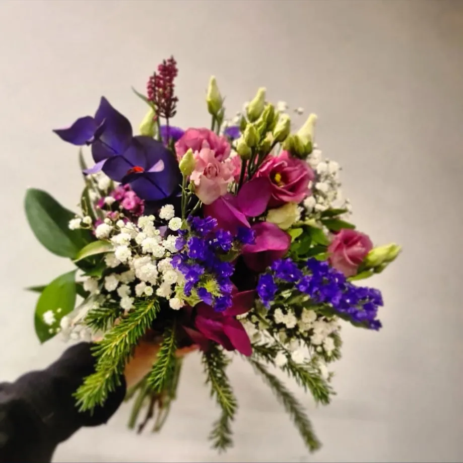 Ramo suave en tonos morado, rosa y blanco sujeto en la mano